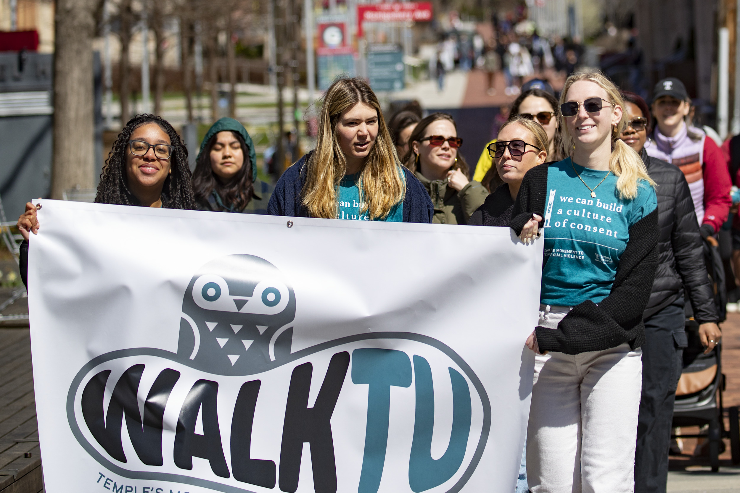 A group of students hold a sign that states "WalkTU" and walk around campus.