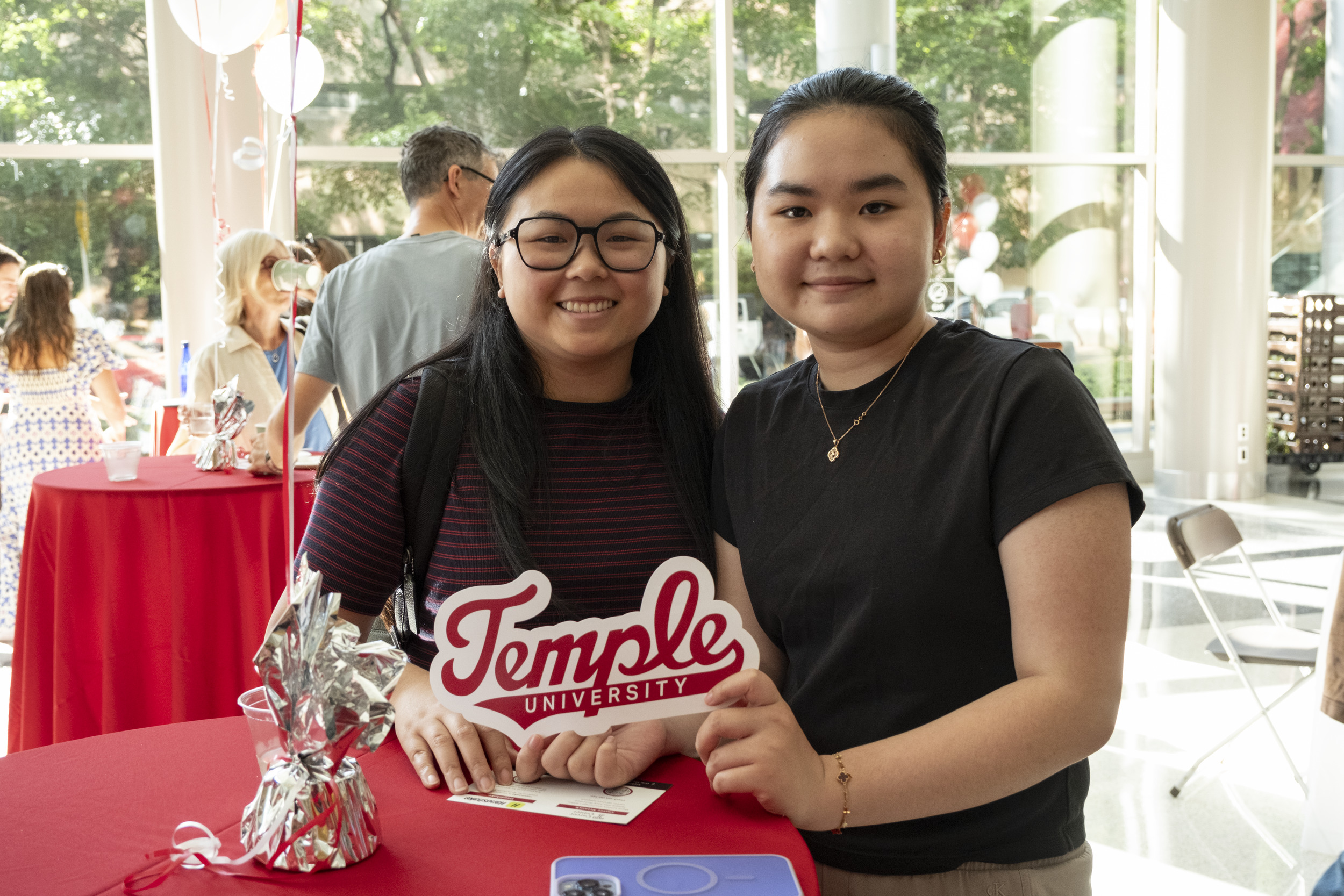 Two temple students pose for a photo holding a Temple sign.