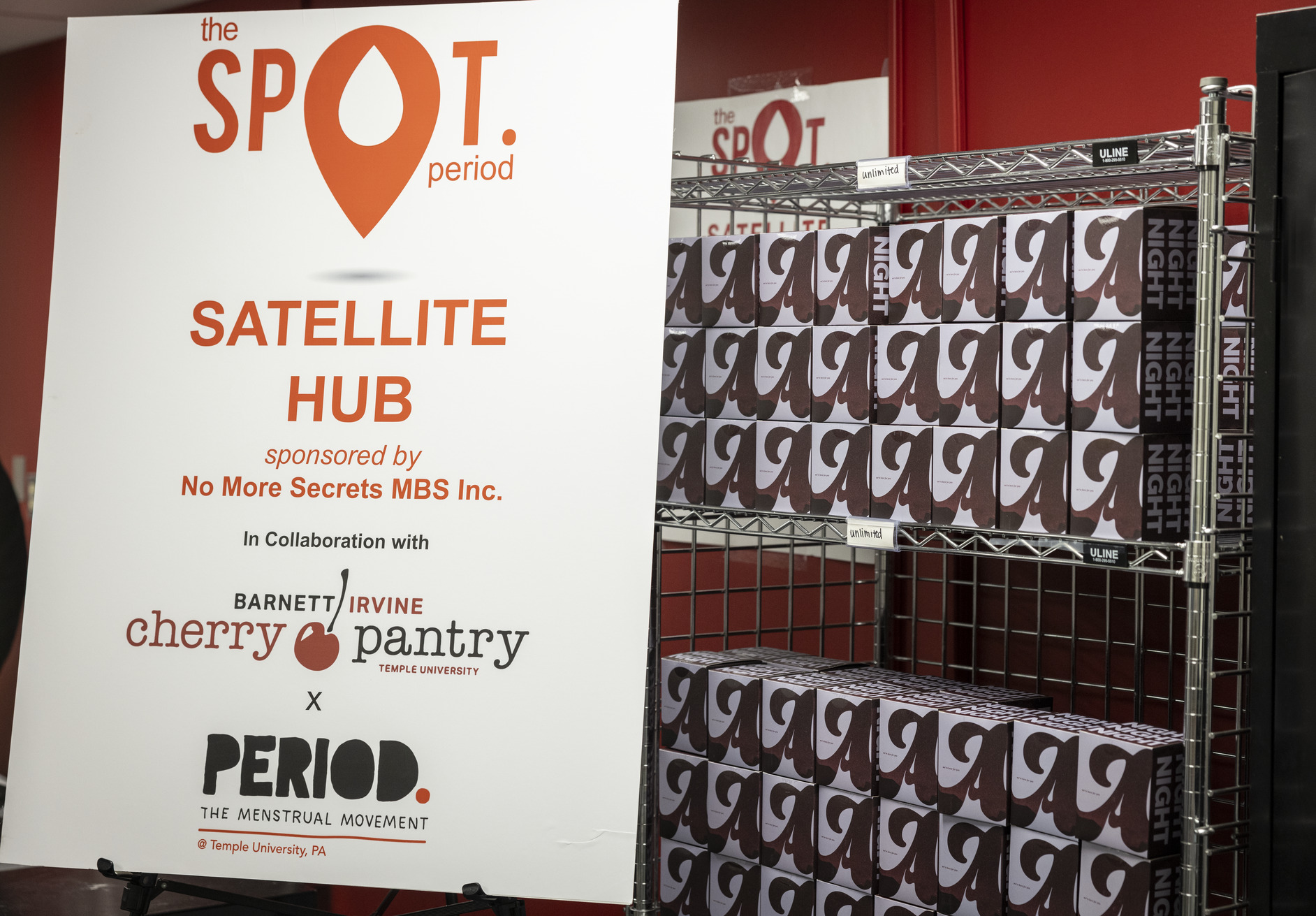 A rack of menstrual hygiene products next to a SPOT Period Satellite Menstrual Hub sign in the Barnett Irvine Cherry Pantry