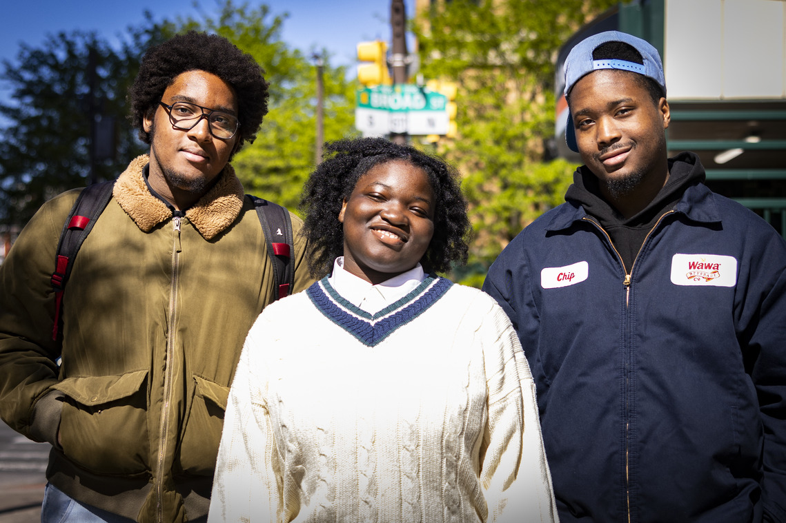 Image of three people standing with trees and a street sign in the background.