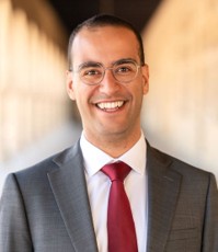 Male with short hair cut, wire frame glasses, gray suit, white shirt and cranberry tieglasses