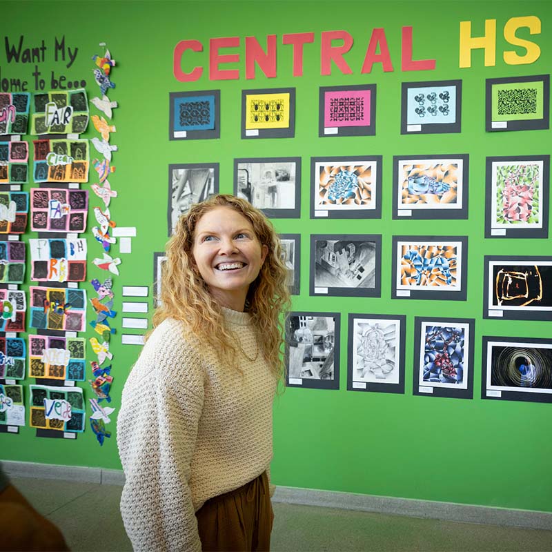 person smiling in front of high school student artwork