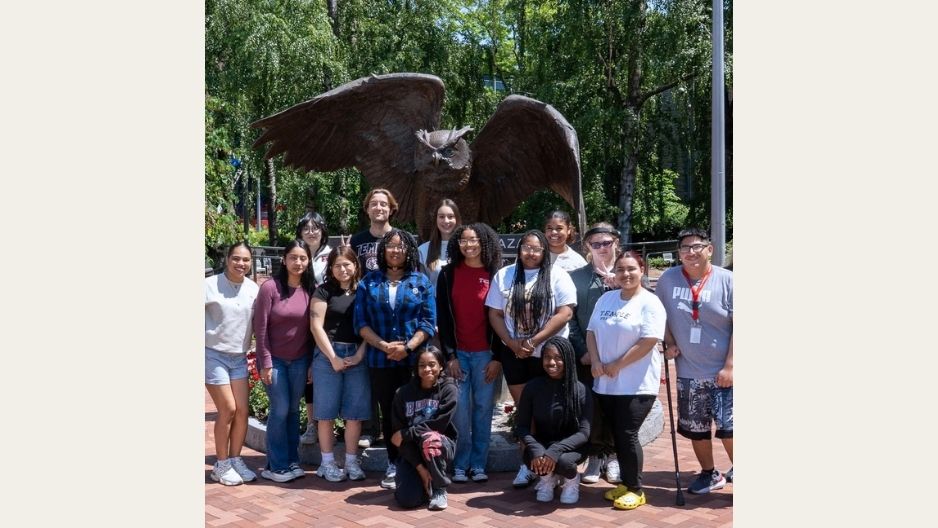 A large group of teens stands together for a group shot in front of an Owl sculpture