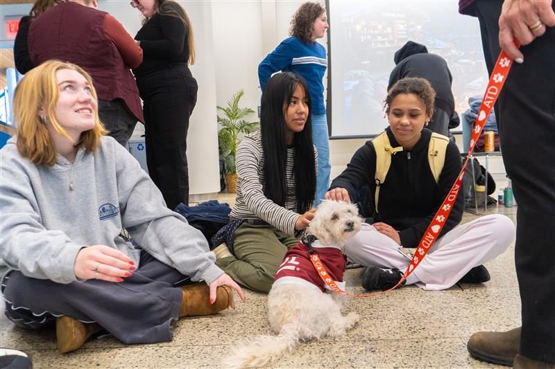 3 students pet a dog in the 1st Floor Event Space at Charles Library. 