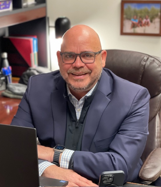 Portrait of David Leach sitting at his desk wearing a dark suit