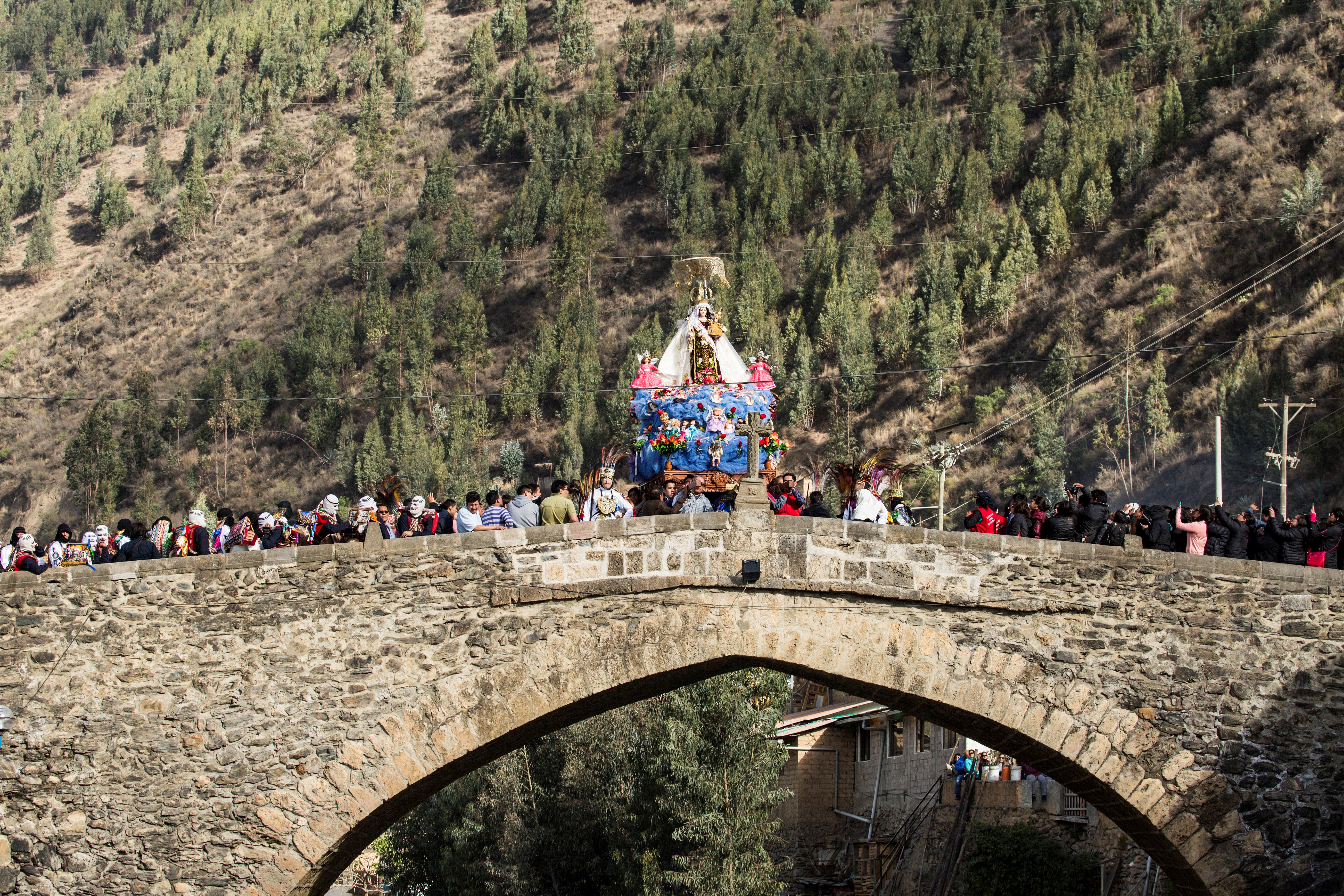 Bridge showing ceremonial procession or celebration. Some individuals dressed in cultural attire. Large groups of people observing.