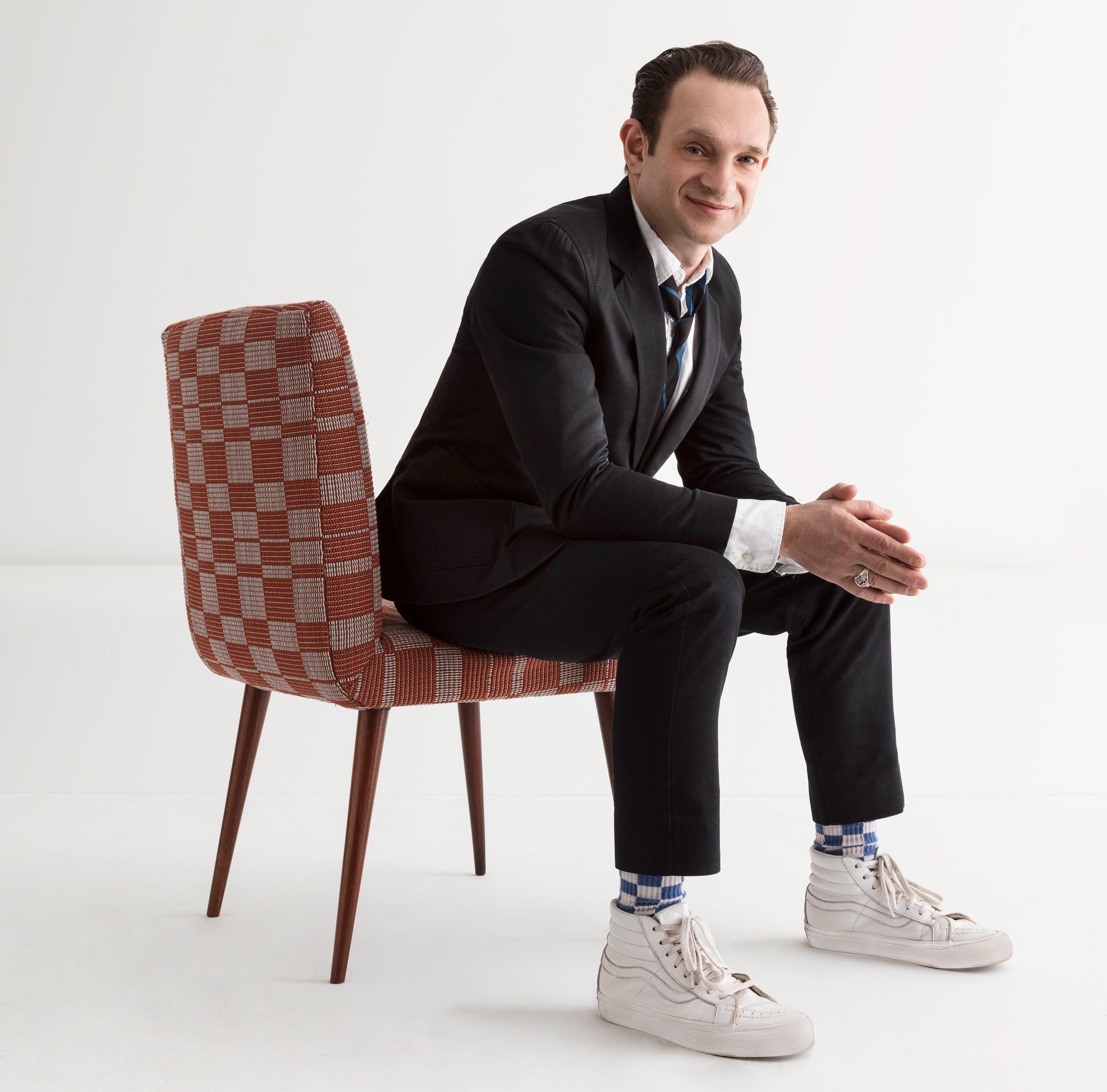Evan Snyderman wears a suit and sneakers. He is seated on a chair in a white studio.
