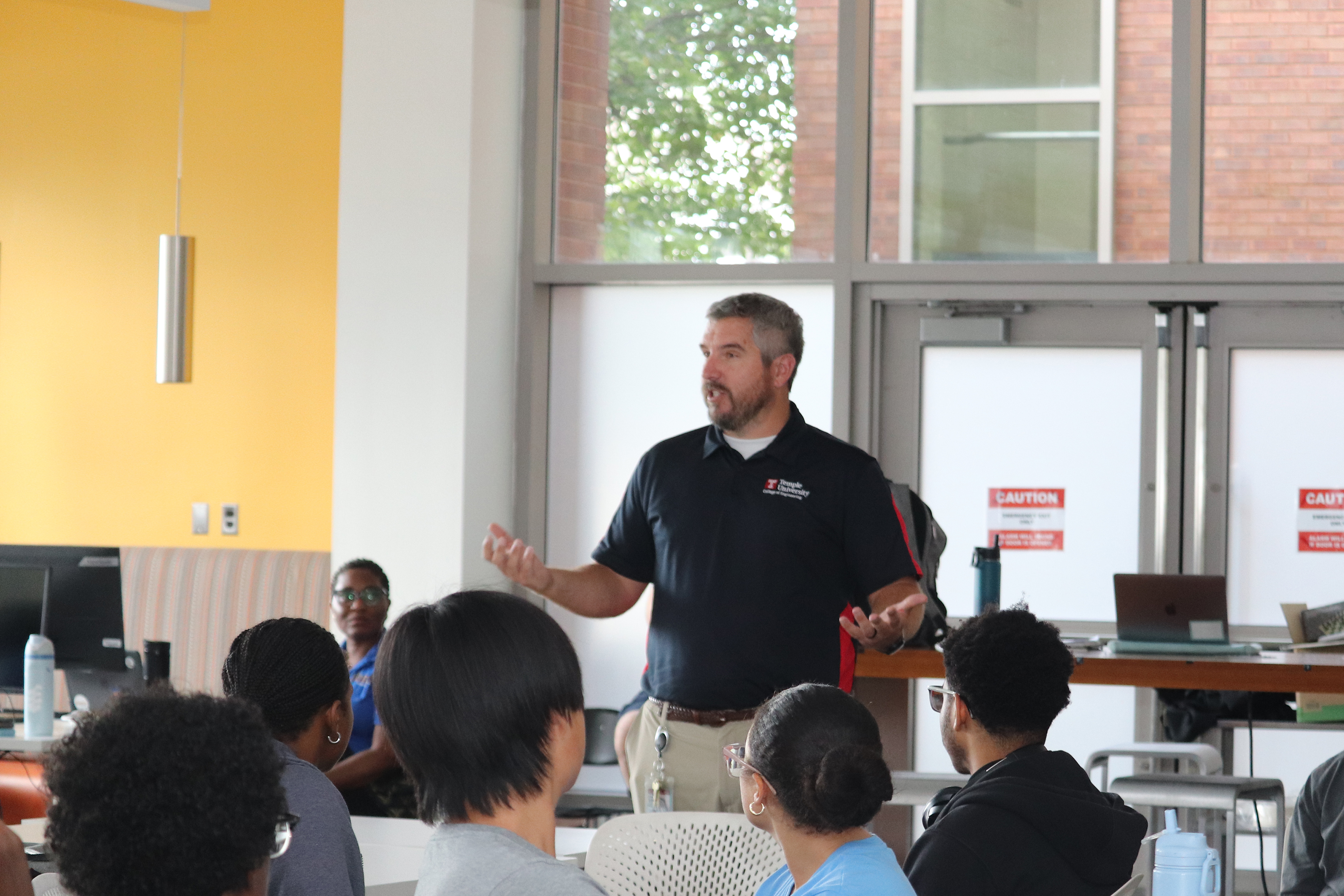 A professor stands in a classroom speaking to a group of students.
