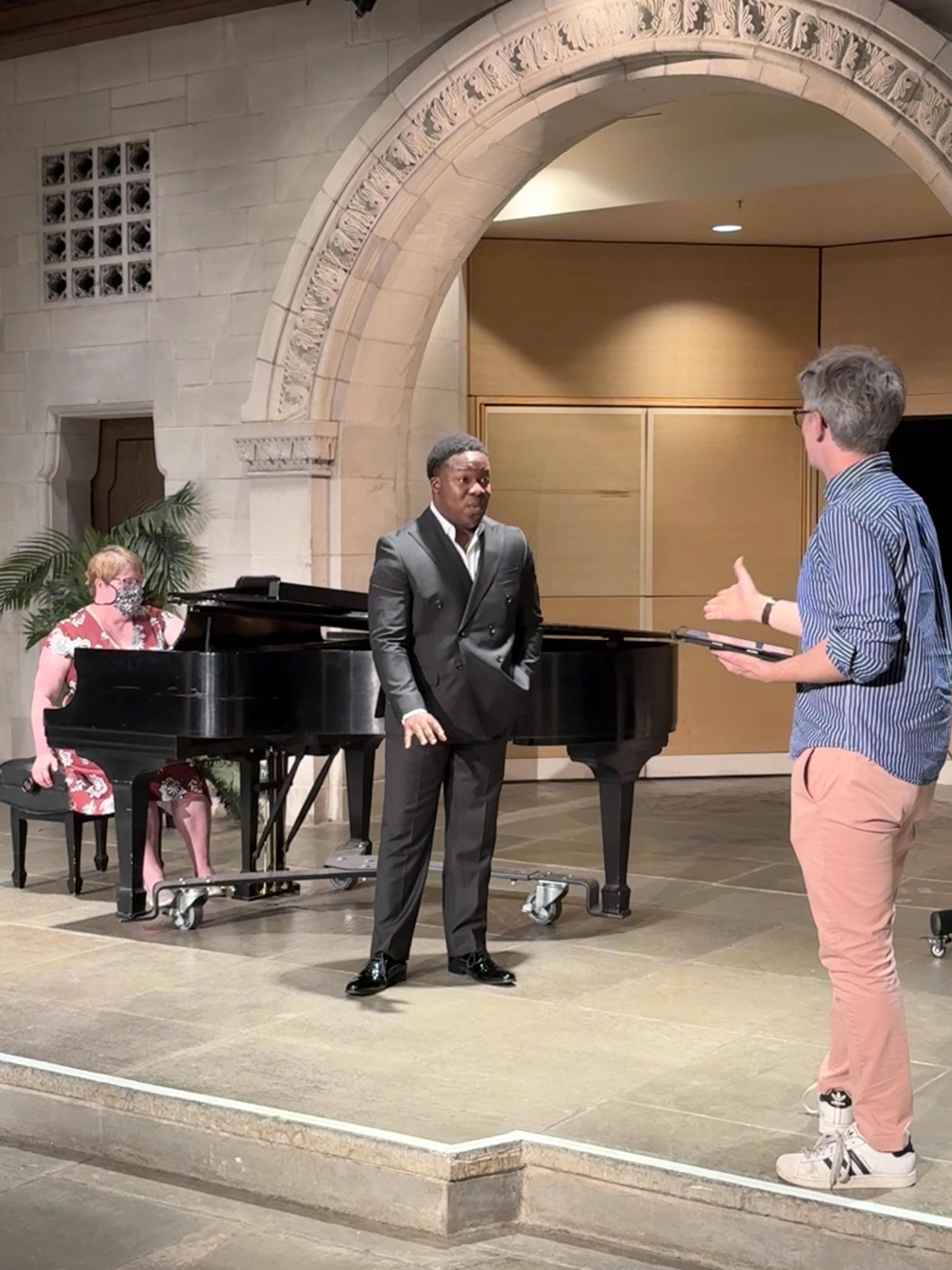 Photo of a student vocalist next to a piano receiving feedback from a guest artist