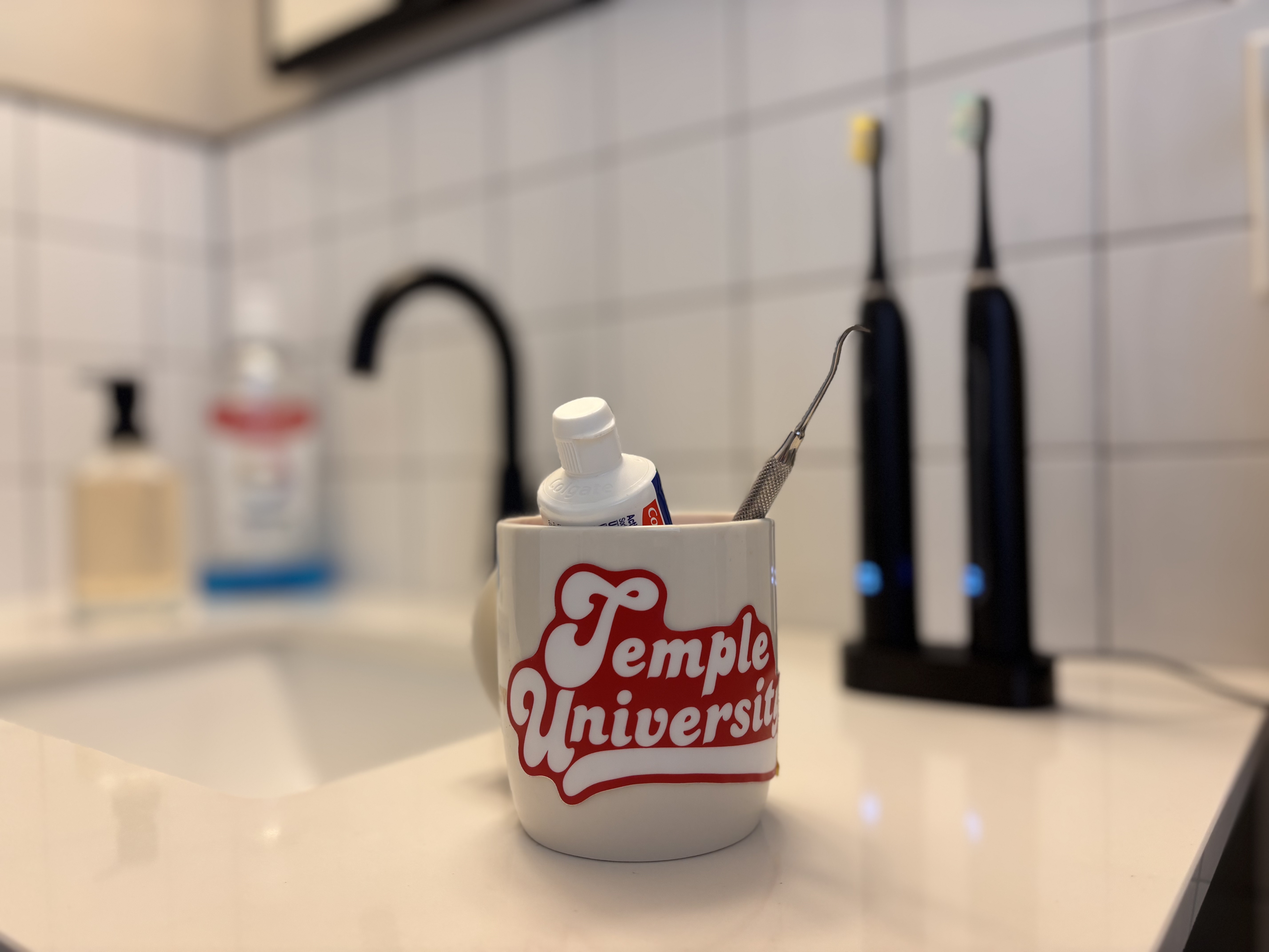 Temple University mug containing oral hygiene tools rests on a bathroom sink.