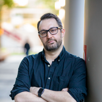 image of Jason wearing a blue shirt and glasses smiling at the camera