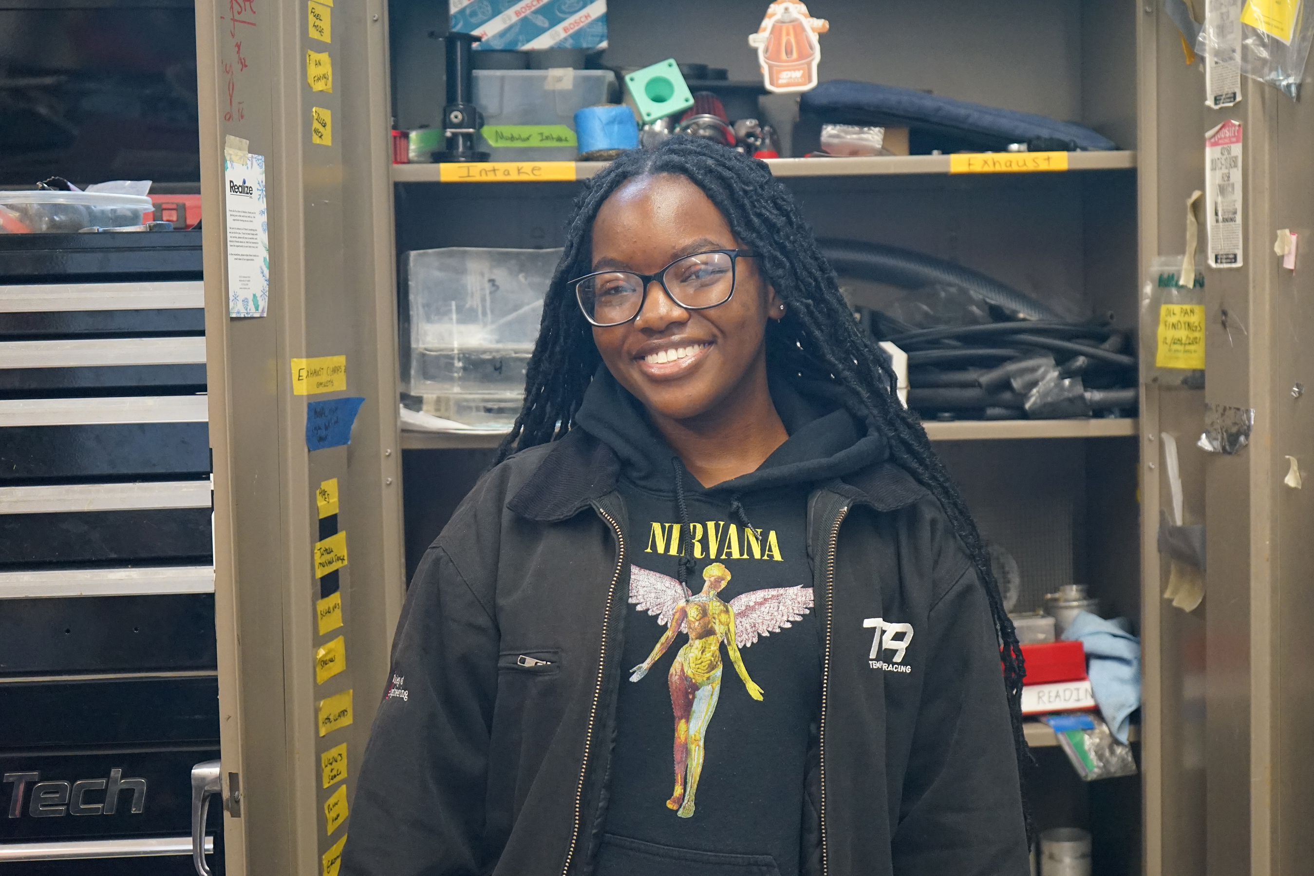 A headshot photo of Kaylah Chambers. She is wearing a black TFR jacket and standing in the TFR workshop in front of an open cabinet.