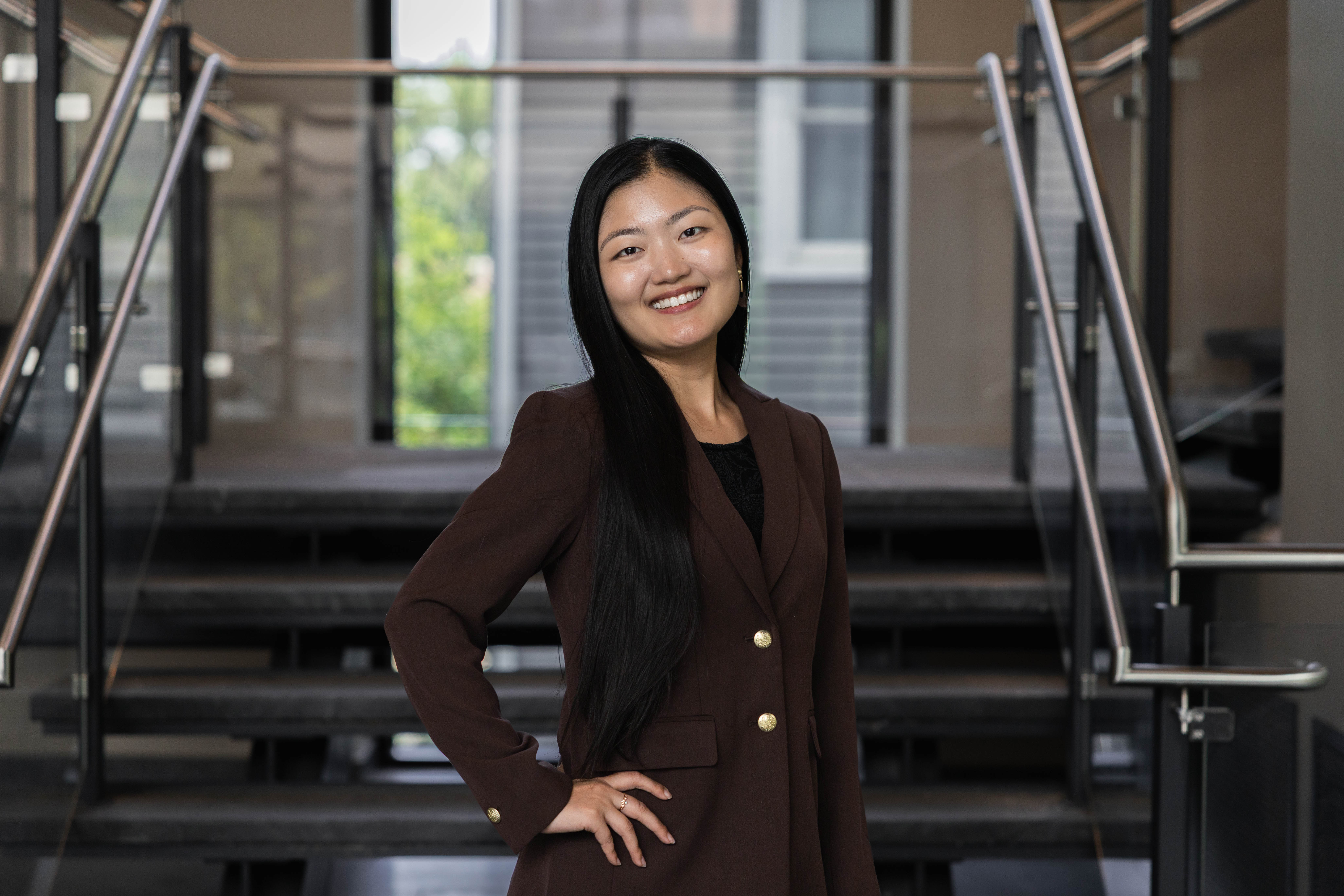 Image of Temple alum standing around a stairwell while wearing a blazer and smiling.