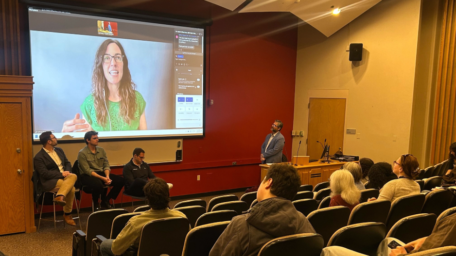 Three person panel speaks to students. A fourth panelist, is present via screen.