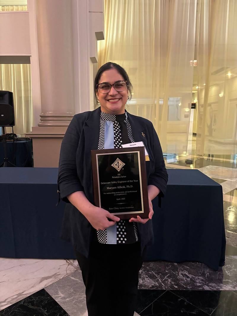 A woman stands in a banquet hall holding a plaque. She is dressed professionally and smiling.