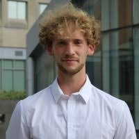 image of Raphael in a white dress shirt standing on the terrace looking at the camera