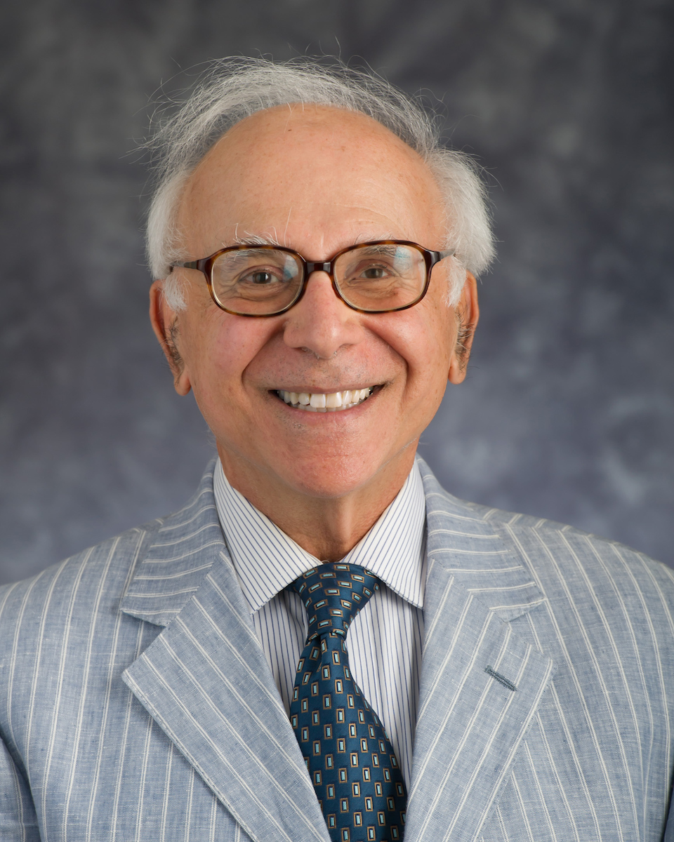 white male wearing glasses short crop grey hair and grey and white suit jacket and tie