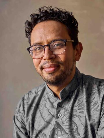 Sebastián Gil-Riaño wearing glasses and a grey shirt smiling at the camera