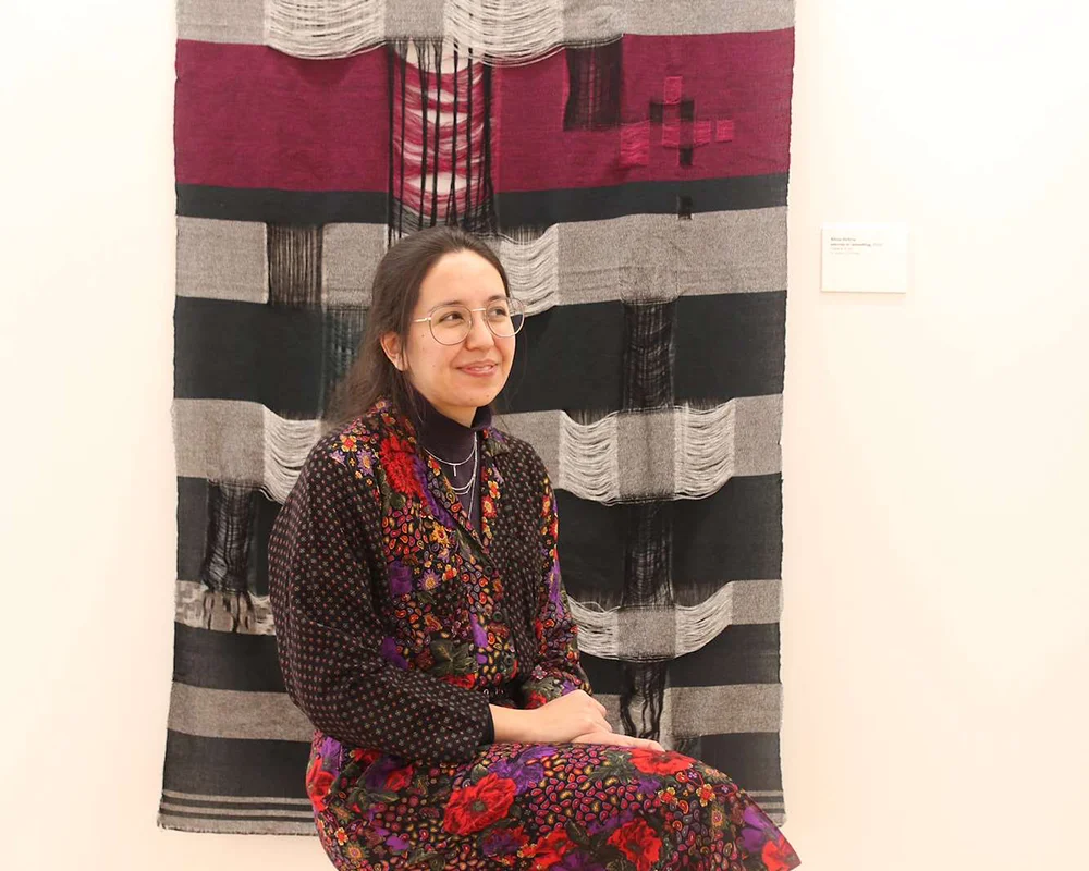 Artist Alicia DeVrio sits in front of her work