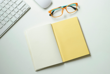White and yellow notebook placed near keyboard and eyeglasses 