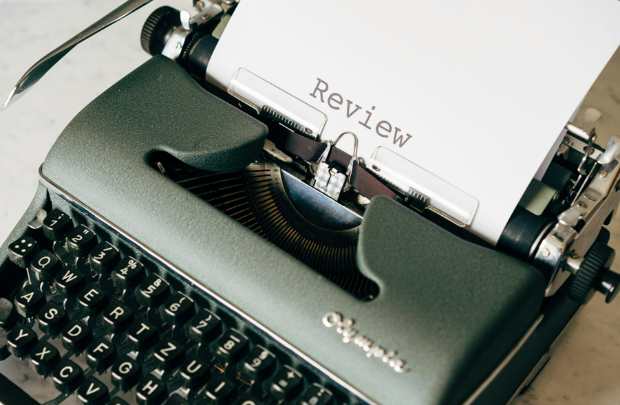Black and White Typewriter on Table, with a piece of paper that says “review” 