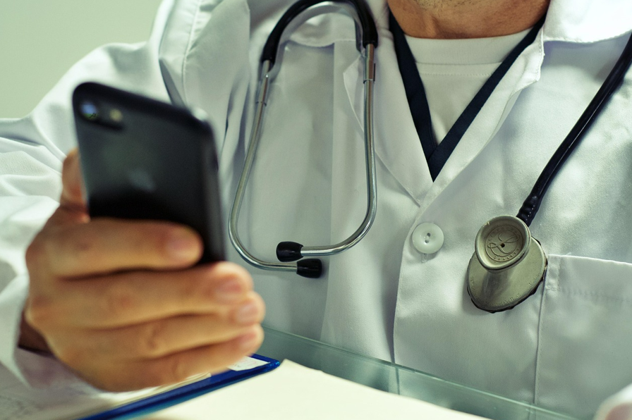 A doctor, seated, holding and using their cell phone 