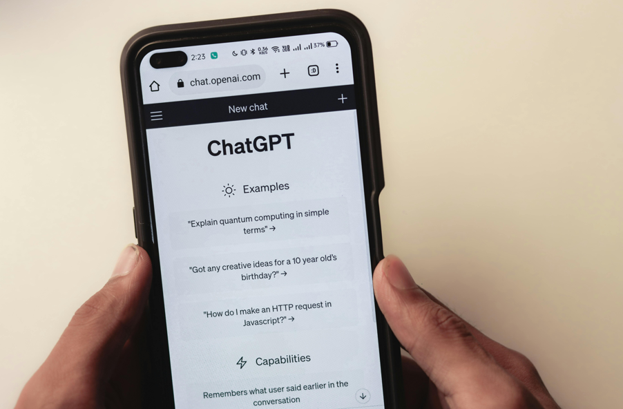 A person holding a smartphone, which is showing the website of ChatGPT, an AI chatbot. 