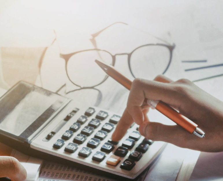 A hand working on a calculator at a busy workspace.