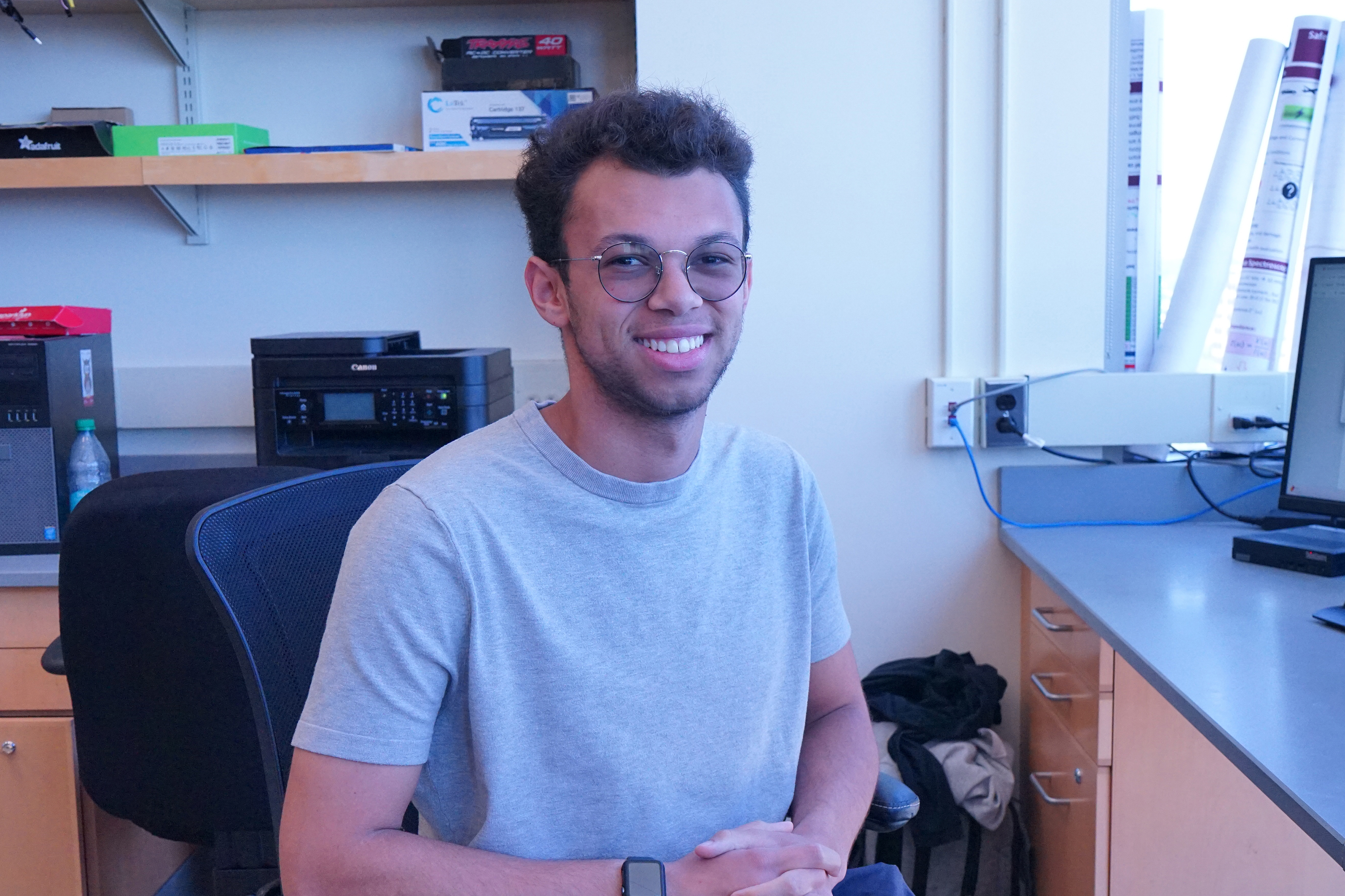 A student is sitting in a computer lab facing forward and smiling.
