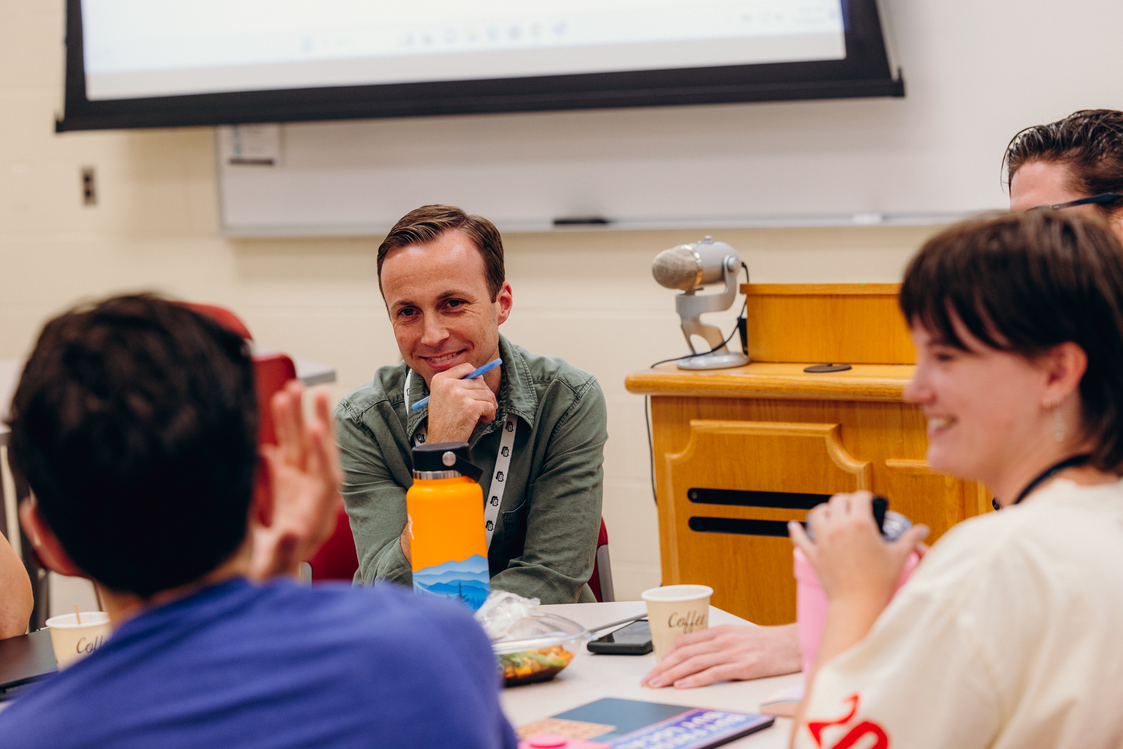 A professor engages students in dialogue at a classroom table