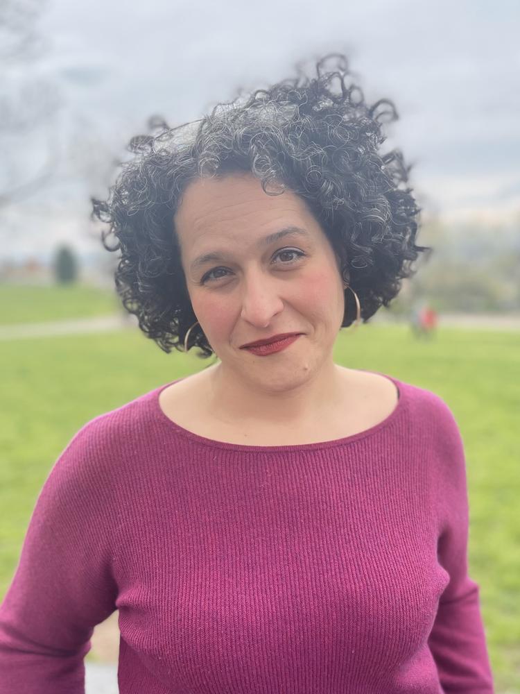 image of Amelia wearing a plum colored shirt standing outside smiling at the camera