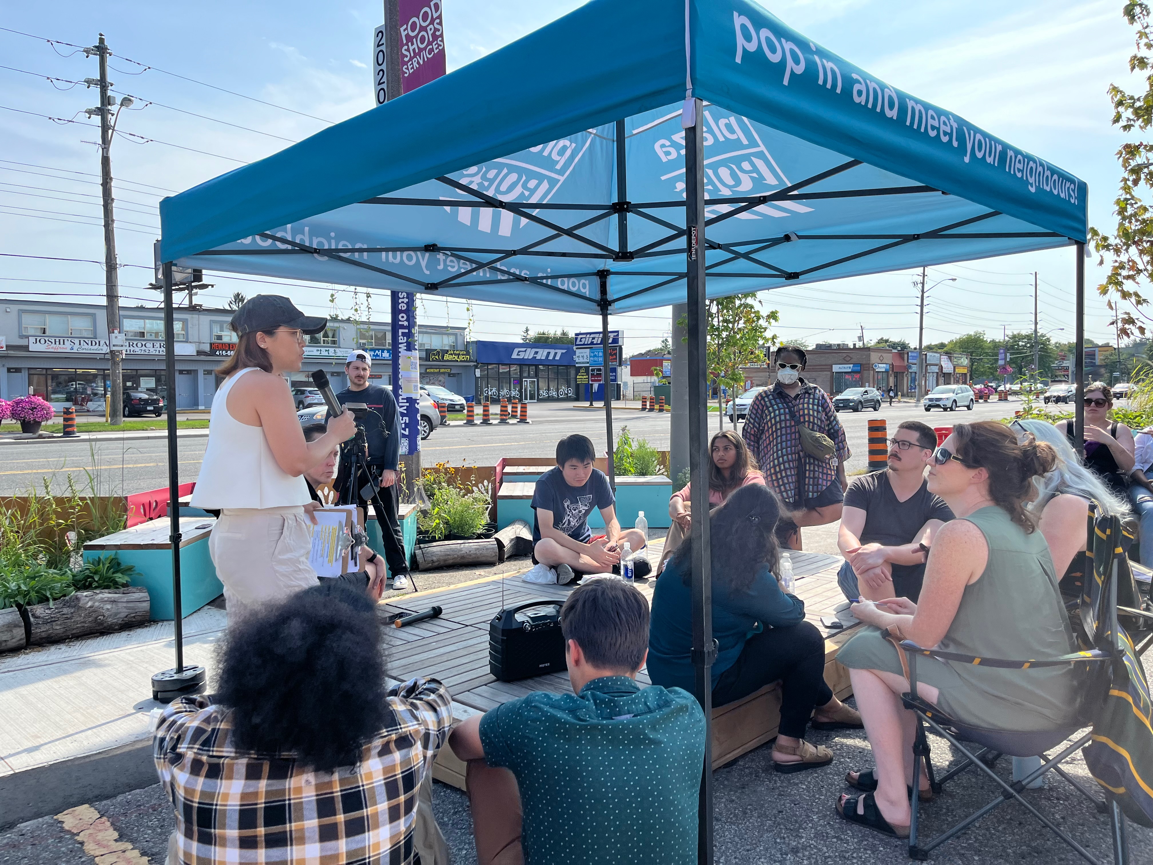 People sit in a circle under a blue tent.