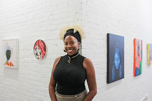 Chelsey Luster stands in front of the art on display in her opening exhibition.