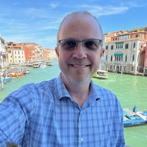 image of Brad standing in Venice wearing glasses and a blue shirt smiling at the camera