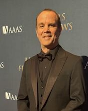 Sergio (Serge) Rey standing in a black suit smiling at the camera