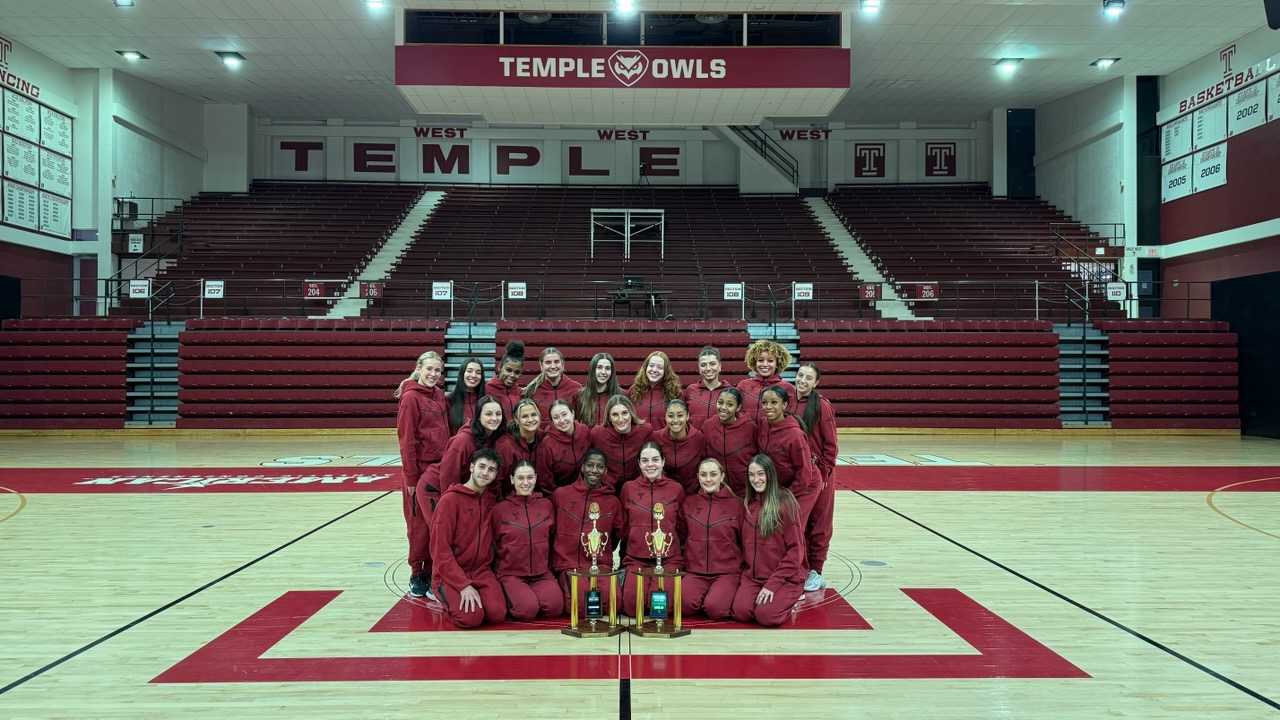 Image of Temple s dance team wearing cherry and white posing in front of trophies.