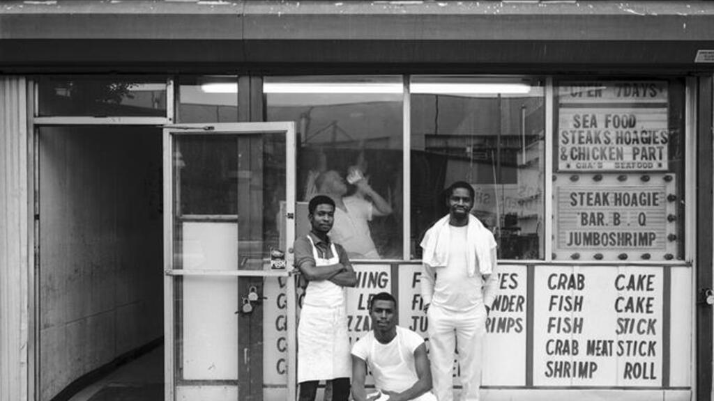 Black and white photo of three men in front of a sandwich shop