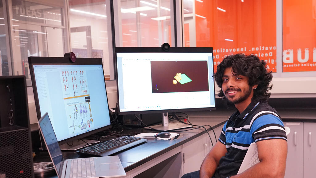 A student sits in a computer lab with research models on the computer screen in the background.