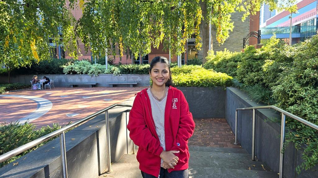 A woman stands with her arms folded in front of her at the brick ramp entrance to Temple University's Founders Garden