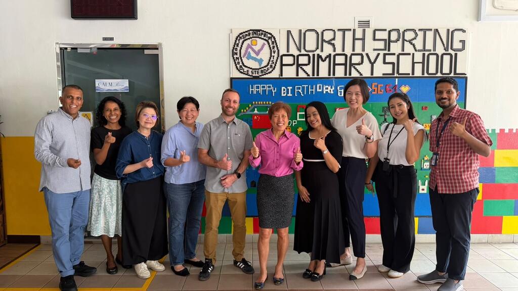 A group of educators and program participants pose together in a school hallway