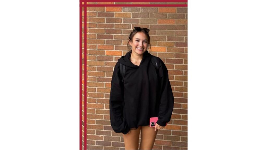 A student stands in front of a brick wall