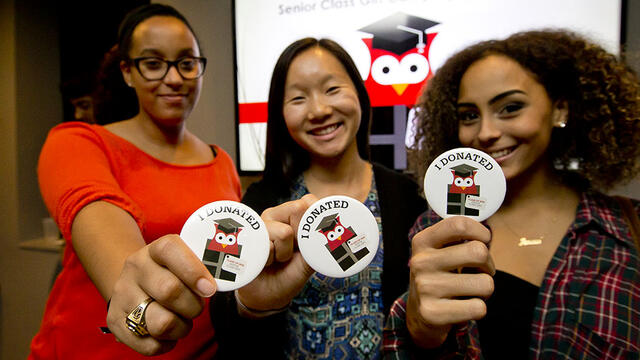 Three students each holding a sticker that says I donated.