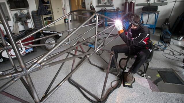 A Temple engineering students welds a portion of a race car.