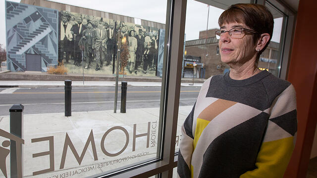 Sister Mary Scullion standing in front of a window, looking out on a mural.