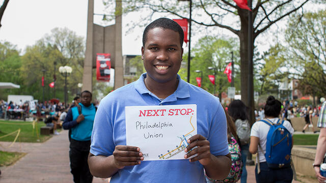 A man in a blue shirt standing in front of Temple s Bell Tower.