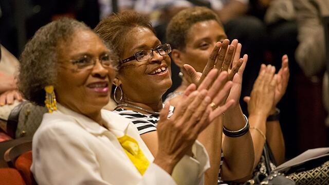 Three women are clapping and smiling.