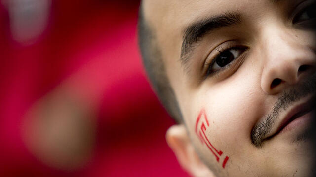 A close up of a man with a red Temple T painted on his face.