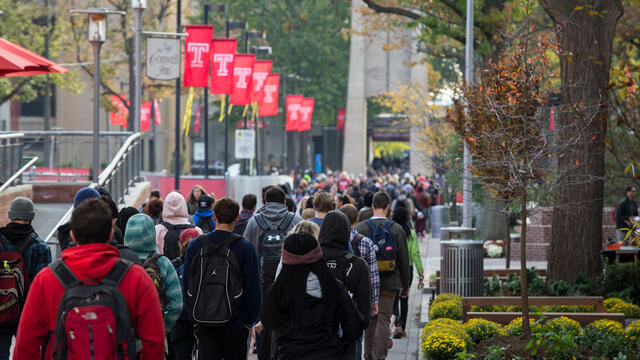 students walking on campus underneath red flags bearing the Temple T .