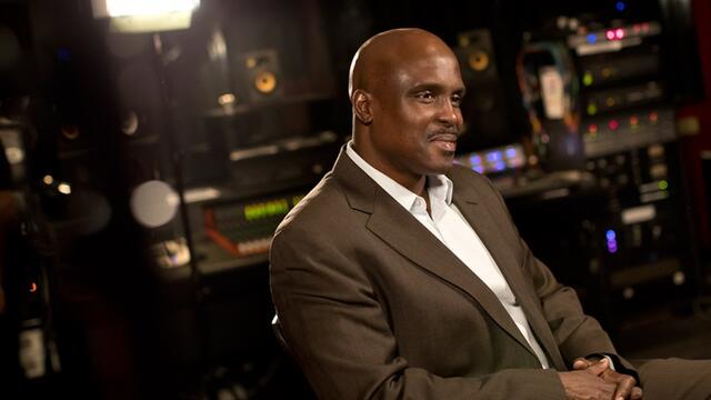 A man in a brown suit sitting in a recording studio.