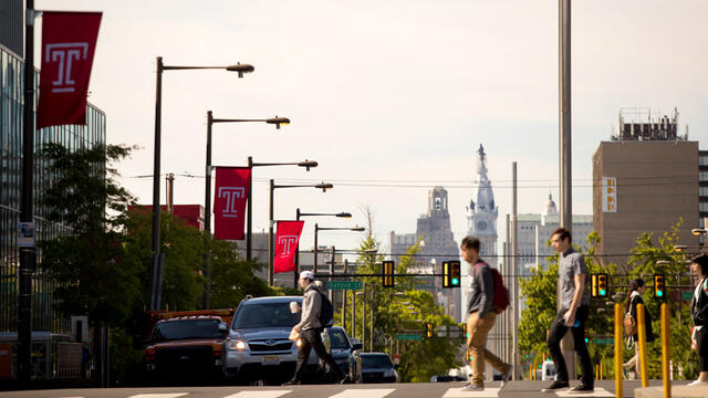 Students crossing Broad Street under red Temple flags.